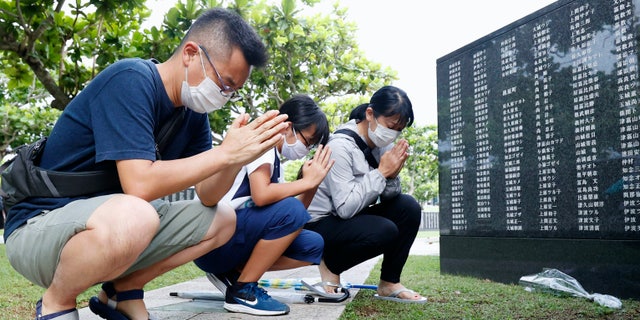 Members of a bereaved family pray in front of a "Cornerstone of Peace" monument wall on which the names of all those who lost their lives, both civilians and military of all nationalities in the Battle of Okinawa are engraved, at the Peace Memorial Park in Itoman, Okinawa, Japan, Tuesday, June 23, 2020. (Kyodo News via AP)