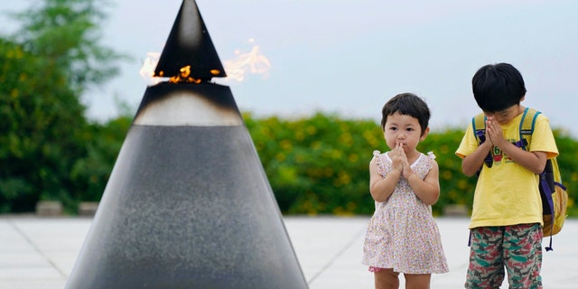 Children pray in front of the "Peace of Fire" at the Peace Memorial Park in Itoman, Okinawa, Japan, Tuesday, June 23, 2020. (Koji Harada/Kyodo News via AP)