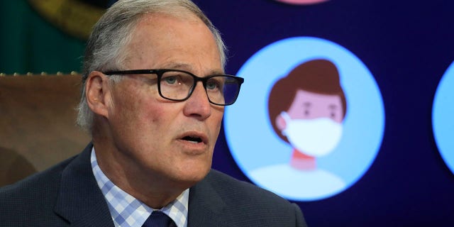 Washington Gov. Jay Inslee speaks next to a video display showing images of people wearing masks during a news conference.