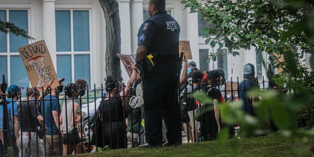 An NYPD officer guarding grounds around City Hall, observe a rally and march Thursday, June 25, 2020, in New York, calling on Mayor Bill de Blasio to defund the NYPD. As the City Council and Mayor's Office put the finishing touches on New York City's 2021 budget, city workers, including Council staff, demand that the fiscal year 2021 budget reduce and reallocate the NYPD operating budget by at least $1 billion. (AP Photo/Bebeto Matthews)