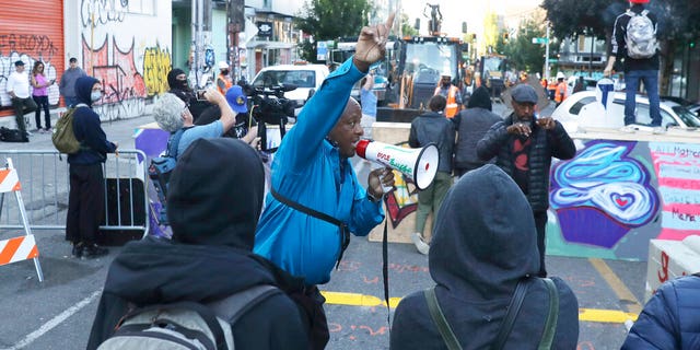 A man speaking in to a bullhorn urges protesters not to be violent after workers and heavy equipment from the Seattle Department of Transportation arrived at the the CHOP (Capitol Hill Occupied Protest) zone in Seattle, Friday, June 26, 2020, with the intention of removing barricades that had been set up in the area. Several blocks in the area have been occupied by protesters since Seattle Police pulled back from their East Precinct building following violent clashes with demonstrators earlier in the month.