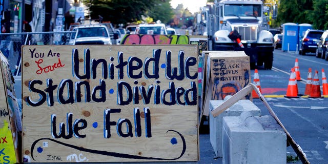 A sign on a barricade reads "United we stand divided we fall," as a truck and other heavy equipment from the Seattle Department of Transportation is staged at the CHOP (Capitol Hill Occupied Protest) zone in Seattle, Friday, June 26, 2020.