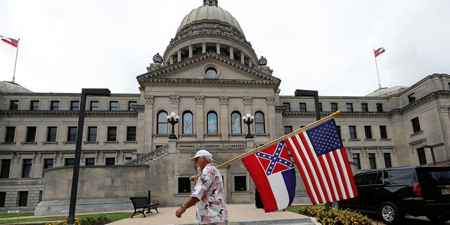 Don Hartness of Ellisville, walks around the Capitol carrying the current Mississippi state flag and the American flag, Saturday, June 27, 2020, in Jackson, Miss. (Associated Press)