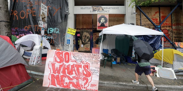 A man walks toward tents in front of a closed Seattle police precinct Saturday, June 27, 2020, in Seattle, where a few streets are blocked off in what has been named the Capitol Hill Occupied Protest zone. (AP Photo/Elaine Thompson)