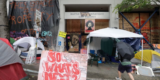 A man walks toward tents in front of a closed Seattle police precinct Saturday, June 27, 2020, in Seattle, where a few streets are blocked off in what has been named the Capitol Hill Occupied Protest zone. (AP Photo/Elaine Thompson)