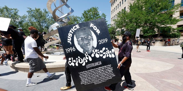 Demonstrators carry a giant placard during a rally and march over the death of 23-year-old Elijah McClain on Saturday outside the police department in Aurora, Colo. McClain died in late August 2019 after he was stopped while walking to his apartment by three Aurora Police Department officers. (AP Photo/David Zalubowski)
