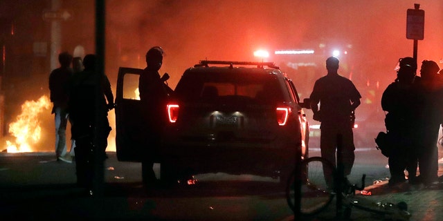 A police car burns, left rear, after being set on fire in Boston, Sunday, May 31, 2020.