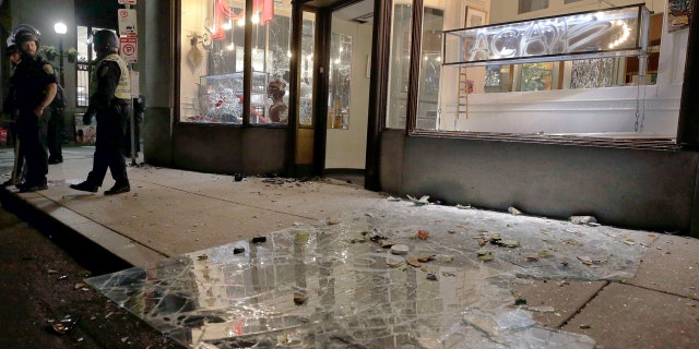 Police officers stand in front of a business with a demolished window in Boston, Sunday, May 31, 2020.