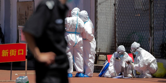 Workers in protective suits check on people's names in a list at a stadium in Beijing, Sunday, June 14, 2020.