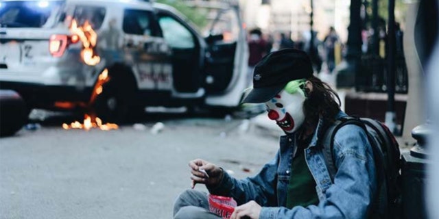 In the images, the masked man can be seen handling a police vehicle’s gas tank and later sitting and posing near the flaming SUV. (Courtesy: DOJ)