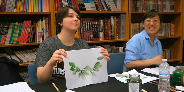 Undergraduate student Moe Lewis, left, shows her watercolor painting of peony leaves at a traditional Chinese painting class at the Confucius Institute at George Mason University in Fairfax, Va., on May 2, 2018. (AP Photo/Matthew Pennington)