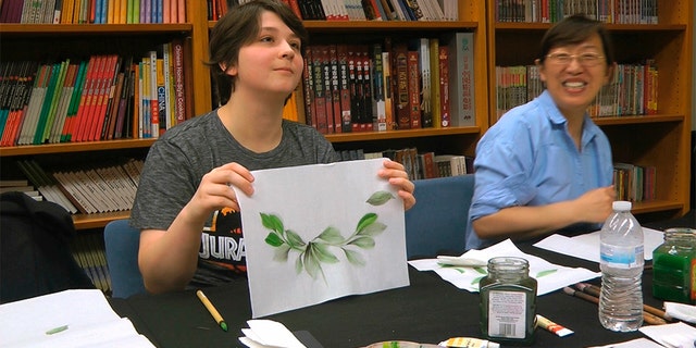 Undergraduate student Moe Lewis, left, shows her watercolor painting of peony leaves at a traditional Chinese painting class at the Confucius Institute at George Mason University in Fairfax, Va., on May 2, 2018. (AP Photo/Matthew Pennington)