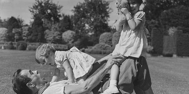Portrait of actor Tyrone Power playing on the grass with his young daughters Romina (right) and Taryn, circa 1955.