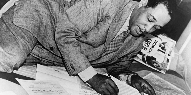 Duke Ellington writing on scores of music. Undated photograph.
