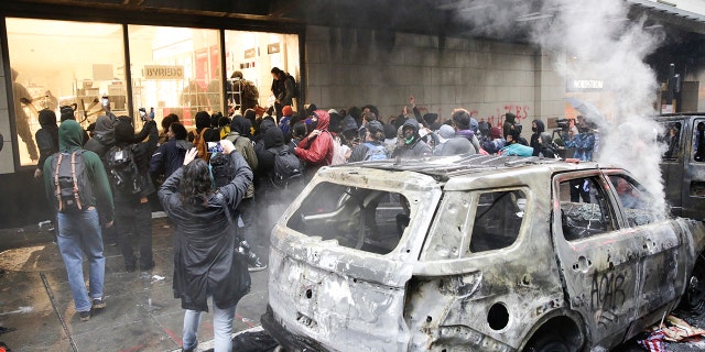 Looters storm a Nordstrom store near a torched police vehicle during a riot in Seattle, May 30, 2020. (Getty Images)