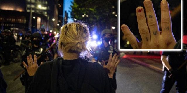 An image shows a woman raising her hands across from police – and in it tattoos on her knuckles are visible. Investigators said those tattoo matched ones they found on Channon when they searched her home. (DOJ)