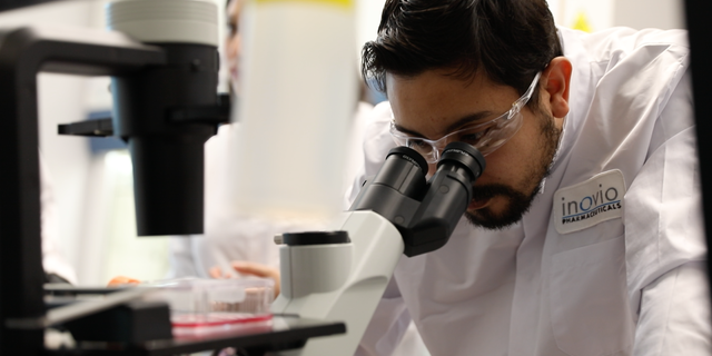 An INOVIO scientist peers into a microscope at the laboratory. (Photo courtesy of INOVIO Pharmaceuticals)