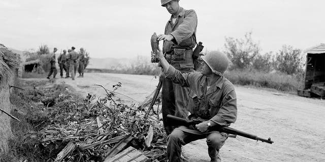 First Lt. John R. Grimes (left) of Milledgeville, Ga., and M/Sgt. George H. Trout of Richland, Pa., examine mortar shells left behind in a roadside ditch by North Koreans hastily fleeing the town of Waegwan in Korea on Sept. 27, 1950. 