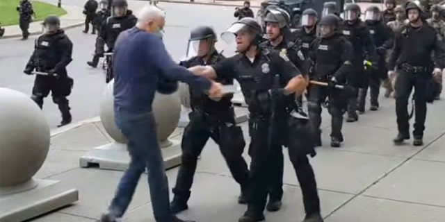 In this image from video provided by WBFO, a Buffalo police officer appears to shove a Martin Gugino who walked up to police. Video from WBFO shows the Gugino appearing to hit his head on the pavement, with blood leaking out as officers walk past to clear Niagara Square. Gugino's lawyer said Thursday that he suffered a brain injury. (Mike Desmond/WBFO via AP)