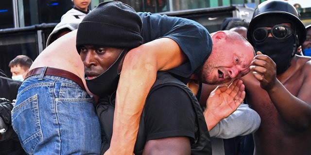 A protester carries an injured counterprotester to safety, near the Waterloo station during a Black Lives Matter protest in London, Britain, June 13, 2020. (REUTERS/Dylan Martinez)