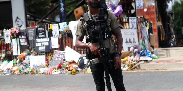 An armed protester awaits the casket of Rayshard Brooks to pass by the area where he was killed near a Wendy's restaurant on Tuesday, June 23, 2020, in Atlanta. (AP Photo/John Bazemore)