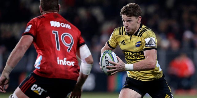 FILE - In this June 29, 2019, file photo, Hurricanes Beauden Barrett, right, runs at Crusaders Luke Romano during the Super Rugby semifinal between the Crusaders and the Hurricanes in Christchurch, New Zealand. The cheers of the crowd will resound in New Zealand sports stadiums for the first time in months with more than 50,000 people expected to attend matches in the opening round of Super Rugby Aotearoa. More than 18,000 are expected at the first match in the New Zealand professional rugby tournament in Dunedin on Saturday, June 13, 2020 between the Highlanders and the Hamilton-based Chiefs. (AP Photo/Mark Baker,File)