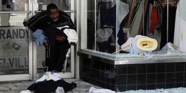 A man exits with clothing from a store Sunday, May 31, 2020, in Santa Monica, Calif., during unrest and protests over the death of George Floyd, who died after being restrained by Minneapolis police officers on May 25.