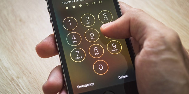 An Apple iPhone5s held in one hand showing its screen with numpad for entering the passcode.