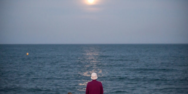 The strawberry full moon, as part of a penumbral lunar eclipse, rises over the horizon as a man sits at Malagueta beach in Spain, June 5, 2020.