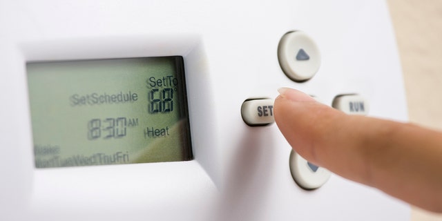 Female hand setting thermostat to 68 degrees Fahrenheit to save energy in the winter.