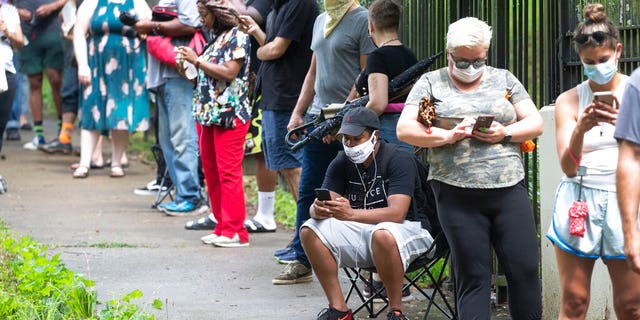 Steven Posey checks his phone as he waits in line to vote, Tuesday, June 9, 2020, at Central Park in Atlanta. Voters reported wait times of three hours. (AP Photo/John Bazemore)