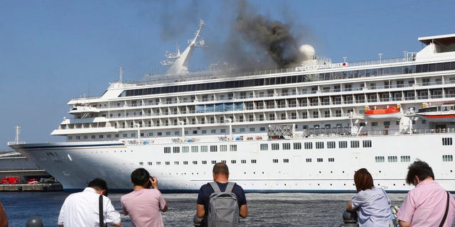 Onlookers watch as smoke rises from the top deck of the Asuka II on Tuesday afternoon in Yokohama.