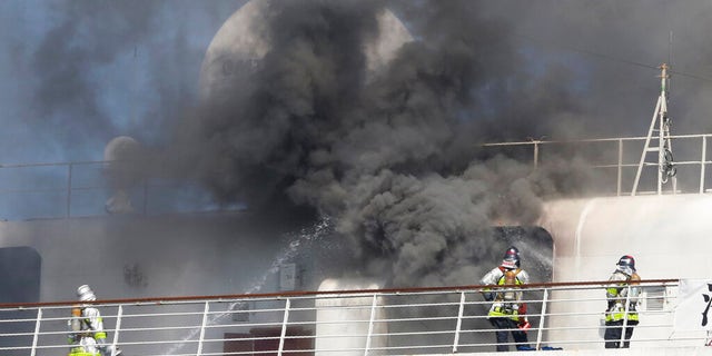 Firefighters are seen battling the fire as black smoke rises from the Asuka II docked at Yokohama Port, near Tokyo.