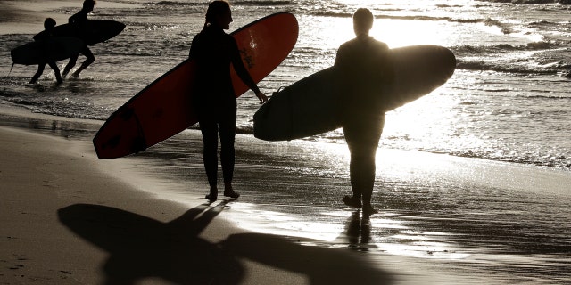 In this April 28, 2020, photo, surfers walk the beach in Sydney, Australia.
