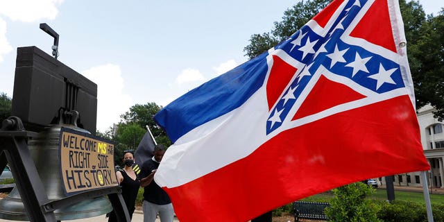 A Mississippi state flag waves adjacent to a flag change supporter's sign that welcomes the state to "the right side of history," outside the Capitol in Jackson, Miss., Sunday, June 28, 2020, while lawmakers are expected to consider state flag change legislation. Mississippi Governor Tate Reeves has already said he would sign whatever flag bill the Legislature decides on. (AP Photo/Rogelio V. Solis)