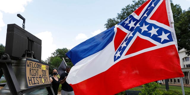 A Mississippi state flag waves adjacent to a flag change supporter's sign that welcomes the state to "the right side of history," outside the Capitol in Jackson, Miss., Sunday, June 28, 2020, while lawmakers are expected to consider state flag change legislation. Mississippi Governor Tate Reeves has already said he would sign whatever flag bill the Legislature decides on. (AP Photo/Rogelio V. Solis)