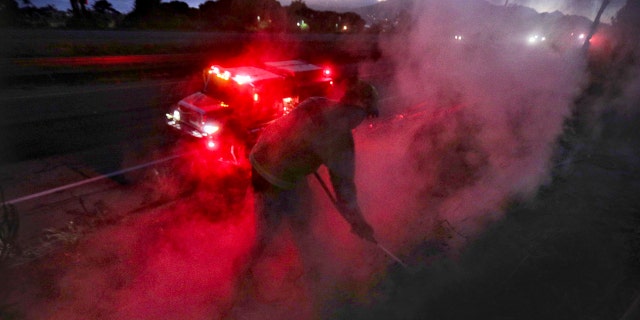 Marcus Anguiano, with the California Department of Forestry and Fire Protection, works on hotspots along U.S. 101 after sunset June 15, in Pismo Beach, Calif.