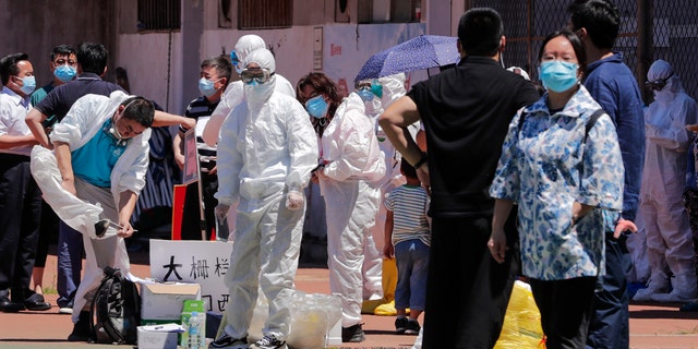 Workers put on protective suits as they wait for people living surrounding the Xinfadi wholesale market arrive to get a nucleic acid test at a stadium in Beijing, Sunday, June 14, 2020.