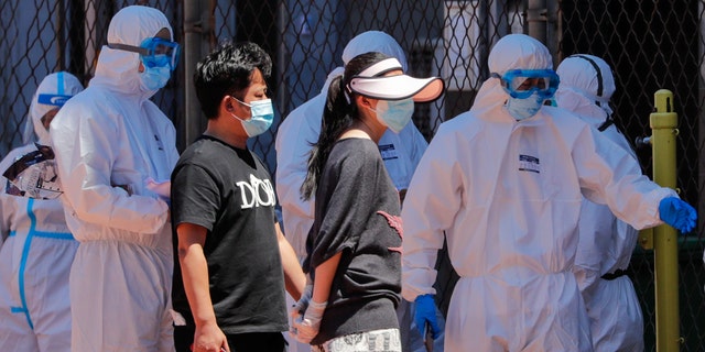 Workers in protective suits direct people who were either living surrounding the Xinfadi wholesale market or have visited the market to get a nucleic acid test at a stadium in Beijing, Sunday, June 14, 2020.