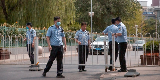 Police officers pull a barricade across a road leading to a residential neighborhood near the Xinfadi wholesale food market district in Beijing, Saturday, June 13, 2020.