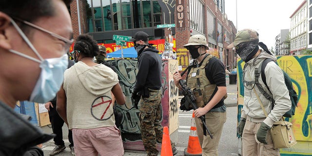 A person who said he goes by the name James Madison, second from right, carries a rifle as he walks Saturday inside what has been named the Capitol Hill Occupied Protest zone in Seattle. Madison is part of the volunteer security team who have been working inside the CHOP zone, and said he and other armed volunteers were patrolling Saturday to keep the area safe. (AP Photo/Ted S. Warren)