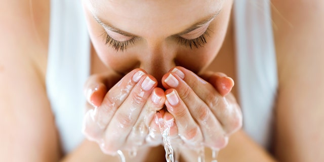 A woman washes her face with water.