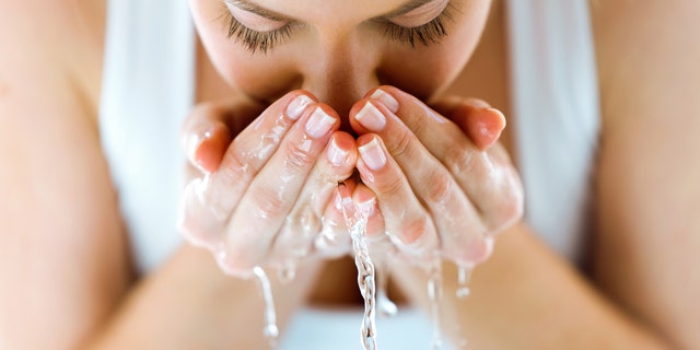 A woman washes her face with water.