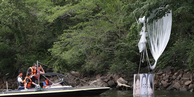 Police officers ride a boat to collect a balloon carrying a banner with images of North Korean leader Kim Jong Un, the late leader Kim Il Sung and Kim Yo Jong, the powerful sister of Kim Jong Un, in Hongcheon, South Korea, on Tuesday. (Yang Ji-woong/Yonhap via AP)