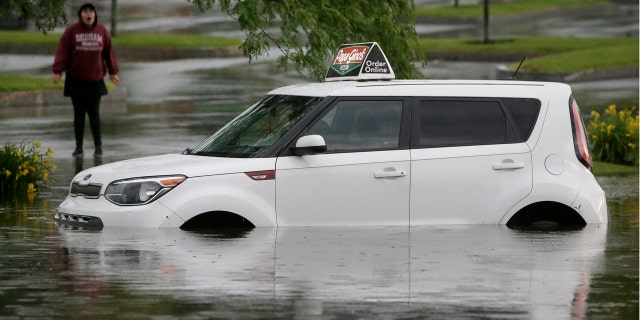 A woman speaks to a person in a vehicle stranded in water, Sunday, June 28, 2020, on a flooded street in Norwood, Mass.