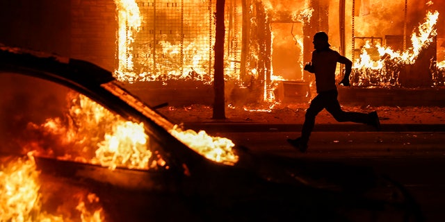 A protester runs past burning cars and buildings on Chicago Avenue, Saturday, May 30, 2020, in St. Paul, Minn. Protests continued following the death of George Floyd, who died after being restrained by Minneapolis police officers on Memorial Day. (AP Photo/John Minchillo)