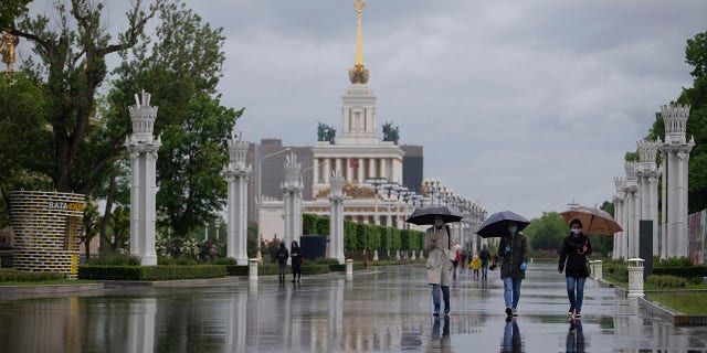 People wearing face masks to protect from coronavirus walk in the rain at VDNKH (The Exhibition of Achievements of National Economy) after reopening in Moscow, Russia, on Monday. (AP Photo/Alexander Zemlianichenko Jr)