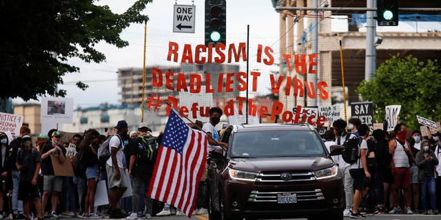 A protester sits out of the window of a car with an American flag as a youth-led protest group walks towards the Seattle Police Department's West Precinct in Seattle, Washington, U.S. June 10, 2020. 