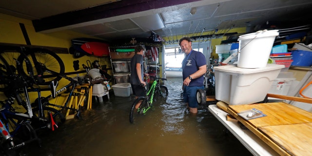 Rudy Horvath Jr., left, moves his bicycle from his home, a boat house in the West End section of New Orleans, as his father, Rudy Horvath Sr., right, looks on after it took on water from a rising storm surge from Lake Pontchartrain in advance of Tropical Storm Cristobal, Sunday, June 7, 2020.