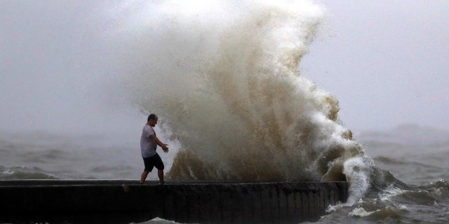A wave crashes as a man stands on a jetty near Orleans Harbor in Lake Pontchartrain in New Orleans, Sunday, June 7, 2020, as Tropical Storm Cristobal approaches the Louisiana Coast.